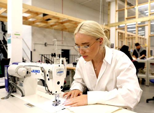 Young woman sat at a table with an industry sewing machine, in a workshop.