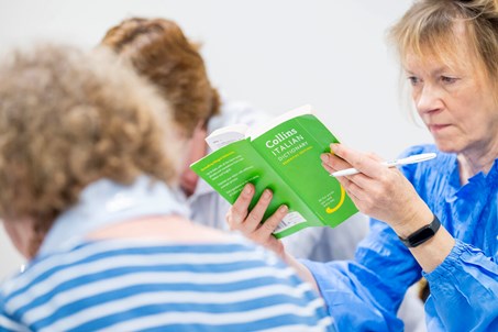 Karen, wearing a blue bouse, reading through a green Italian Dictionary, in her Italian class.