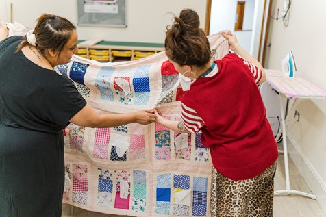 Salima and Tutor Molly holding up and admiring Salima's quilt
