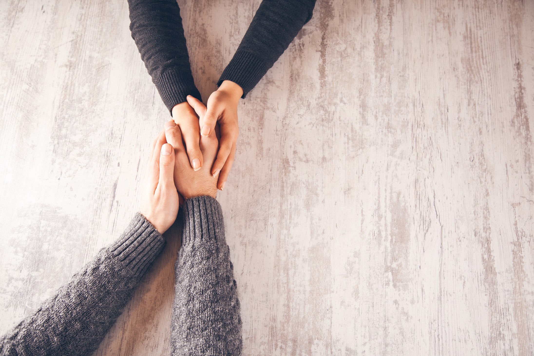 Hands grapOne person holding another’s hands across a table, showing comfort and support.