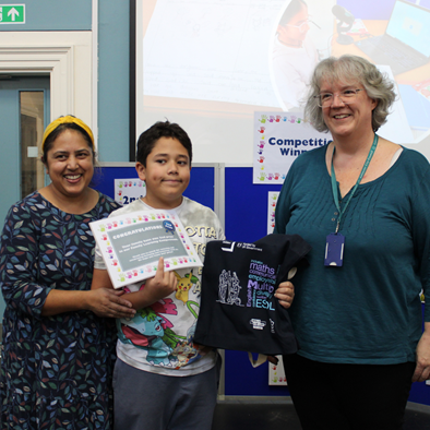 Winner, Jayden holding his prize, next to his mum on the left and Kerry Gray on the right. They are standing in front of the board, showing his entry.