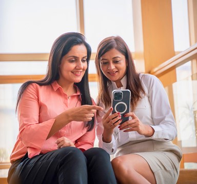 Two females, in smart clothes, looking at a mobile phone together.