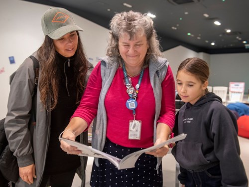 Mother and daughter reading book with library staff
