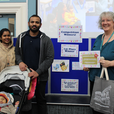 Kerry, Head of Service, with winning Family. They are stood in front of a board and Kerry is passing them a certificate.